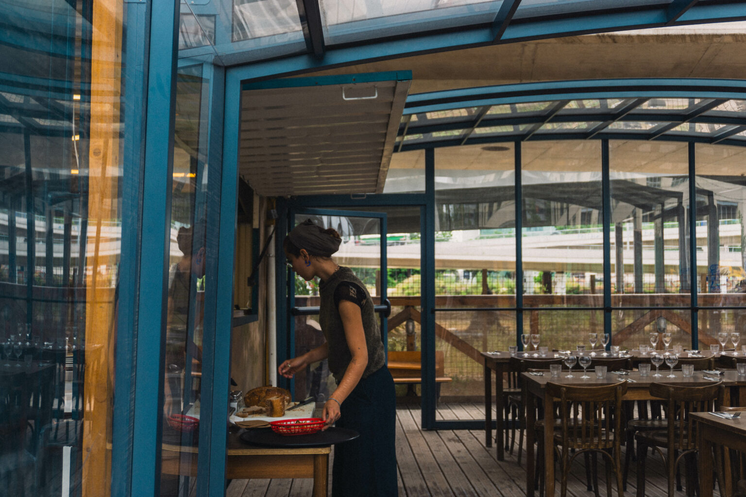 Terrasse extérieure de restaurant couverte par une structure en métal et en verre, serveuse, liaison douce