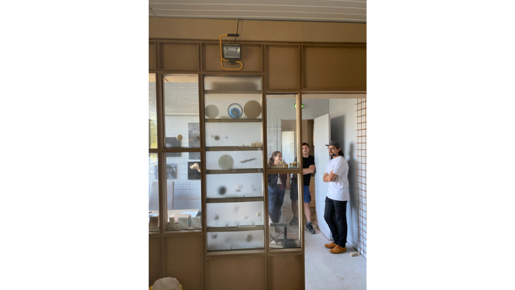 trois personnes debout, étagères en bois et mur en plexiglas