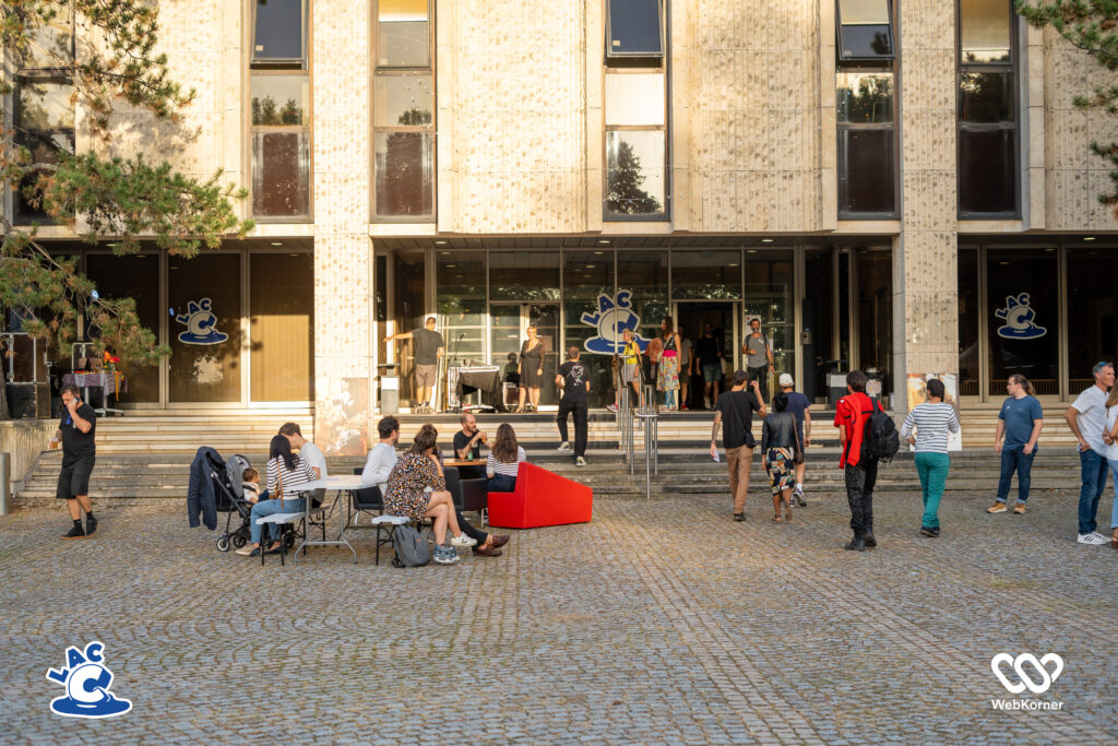 batiment, ciel couchant, personnes assises et debout, canapés, parvis en pavés