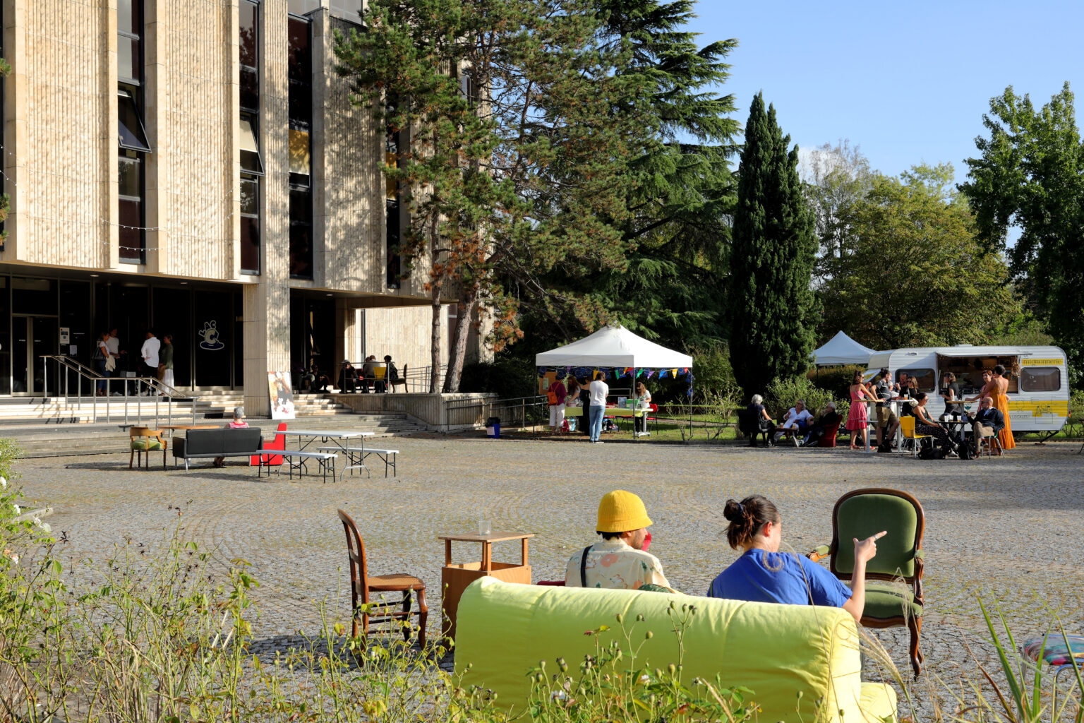 batiment, ciel bleu, personnes assises et debout, canapés, parvis en pavés